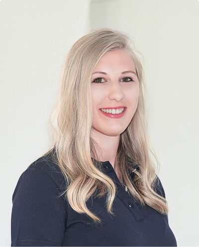 Woman with long blonde hair smiling at the camera, wearing a dark polo shirt against a light background.