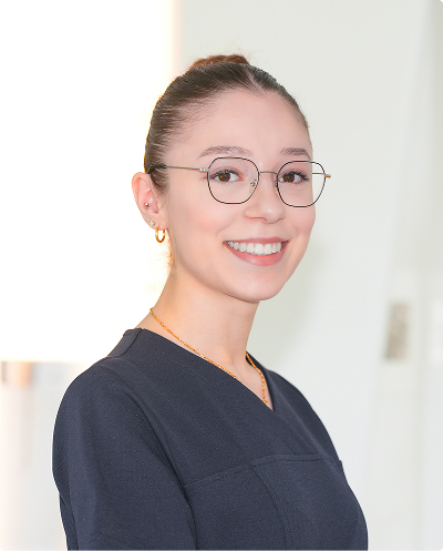 Smiling woman with glasses wearing navy scrubs, posing in a bright, neutral setting.