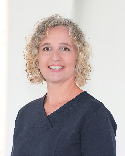 Portrait of a smiling woman with blonde curly hair wearing navy scrubs, looking at the camera.